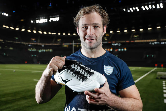 Antonie Claassen tenant une paire de chaussures crampons rugby Wizwedge blanches dans un stade